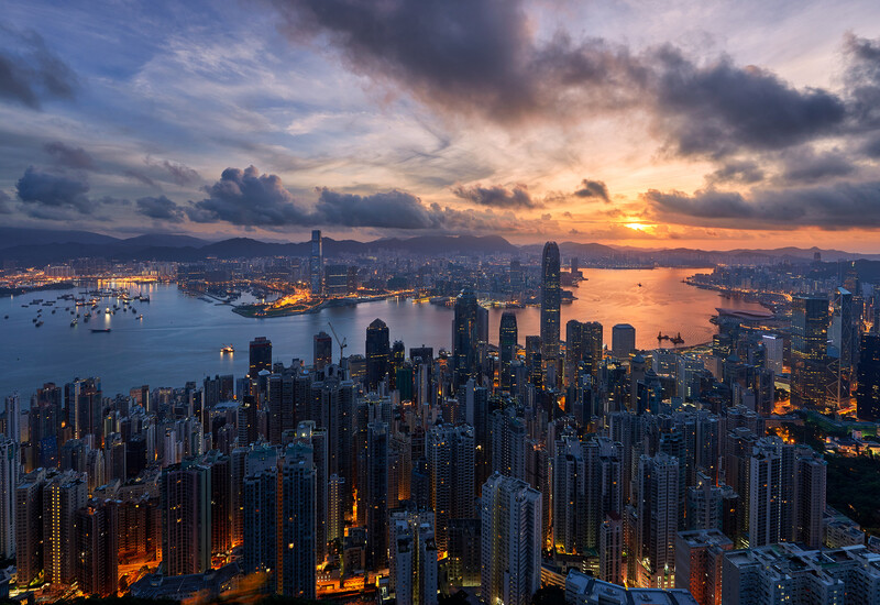 Dense urban skyline at dusk with illuminated buildings reflected in water below.