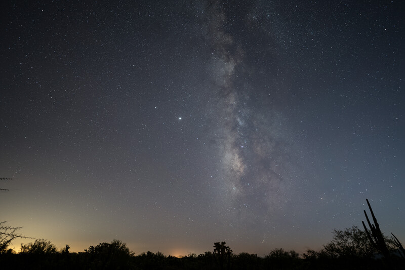 Milky Way galaxy stretching vertically across a night sky above a dark desert landscape at twilight.
