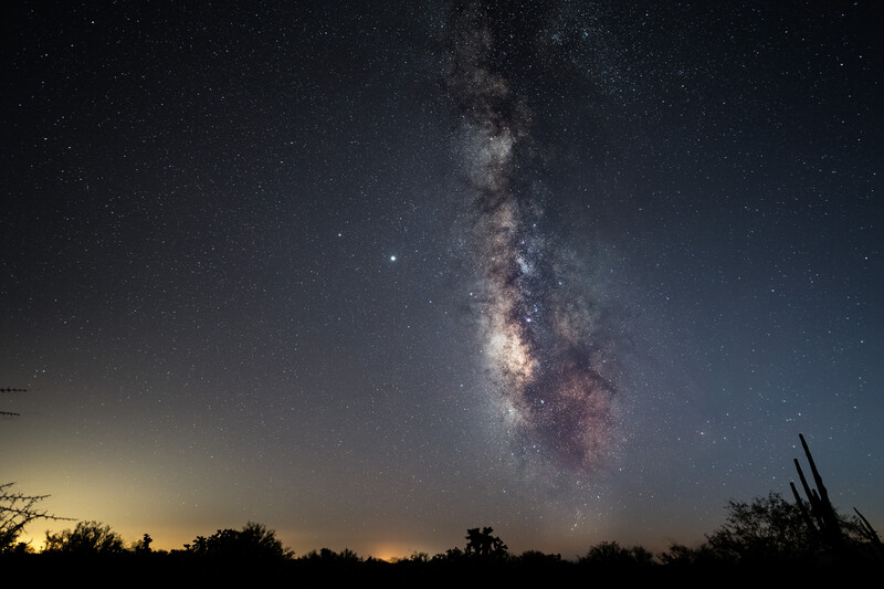 Milky Way galaxy stretching vertically across a dark night sky above a silhouetted desert landscape.