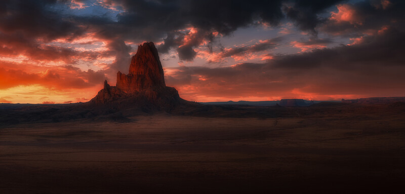 Dramatic sunset over desert rock formation silhouetted against orange and dark clouds.