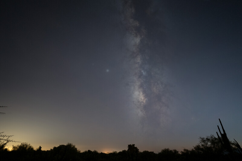 Milky Way core stretches vertically across twilight sky above dark desert landscape silhouette.