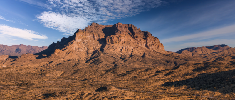 Rugged desert mountain with layered rock formations under clear blue sky.