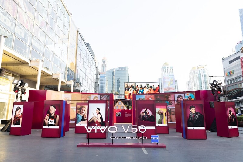 Urban public display installation with burgundy structural elements and portrait photographs arranged in a plaza.