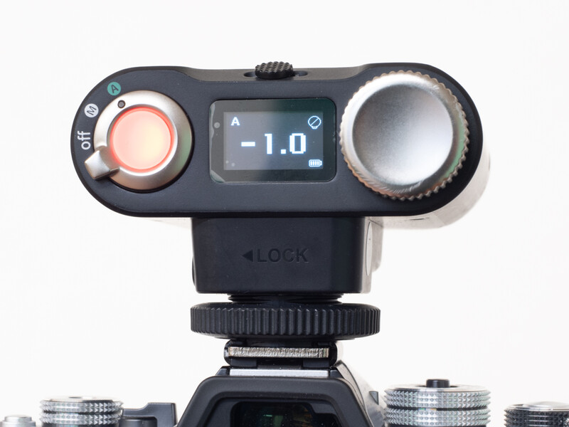 Exposure metering device mounted on camera hot shoe, displaying -1.0 aperture value on LCD screen.