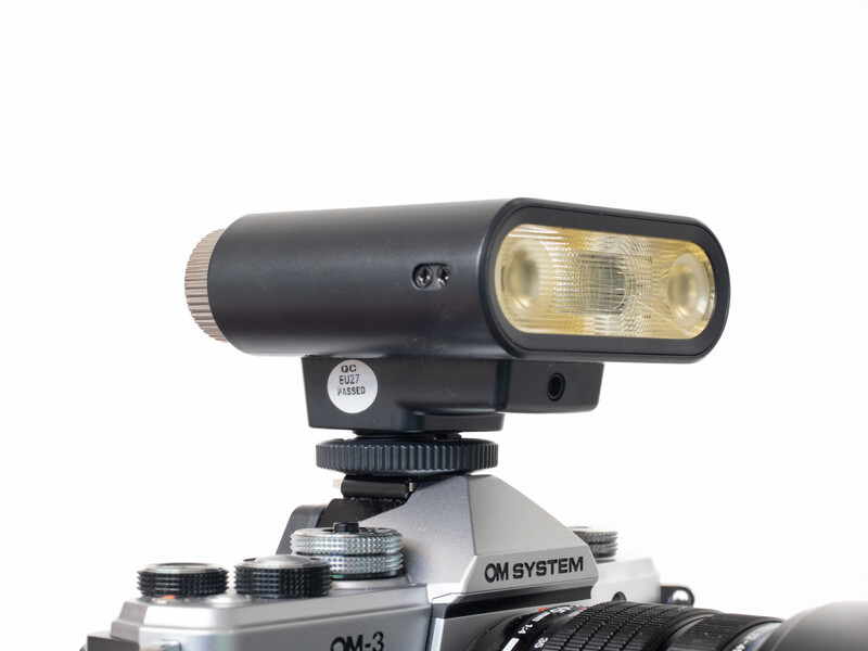 Flash unit mounted on camera hot shoe with diffuser attachment and control dial visible.