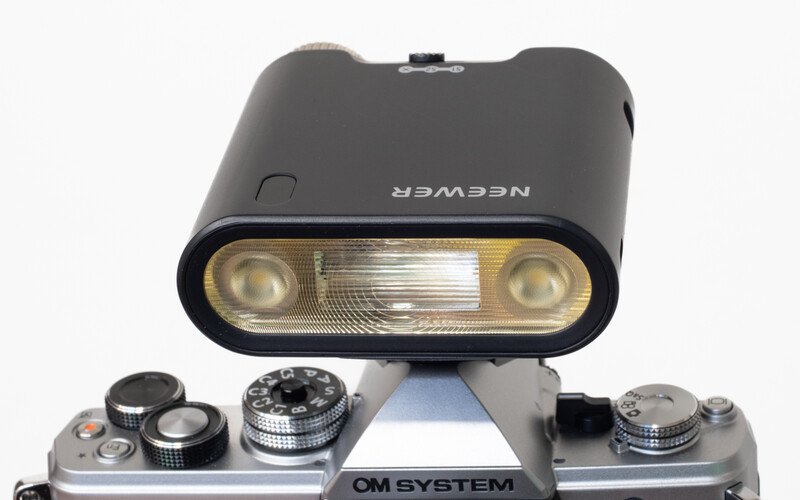 Neewer camera flash mounted on vintage OM system film camera body with manual controls.