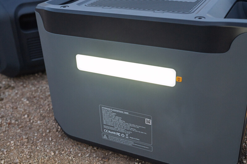 Portable power station with illuminated display panel sitting on gravel ground.