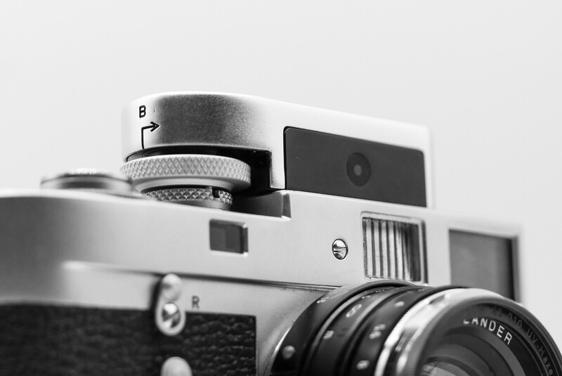 Black and white close-up of a rangefinder camera with lens attached, showing mechanical details and focus mechanisms.
