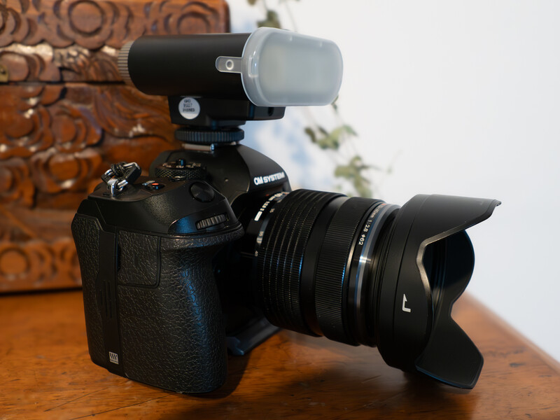 Canon DSLR camera with wide-angle lens and external flash mounted on wooden surface.