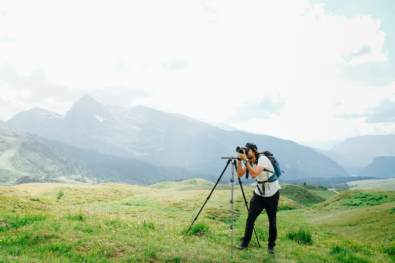 Photographer using tripod and telephoto lens in mountainous valley landscape.