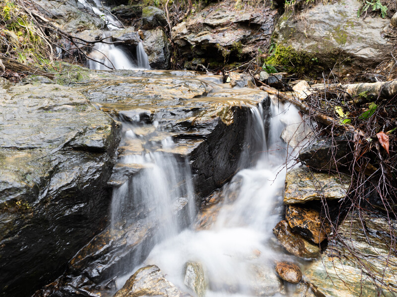 Multi-tiered waterfall cascading over layered slate rocks with silky water motion blur.