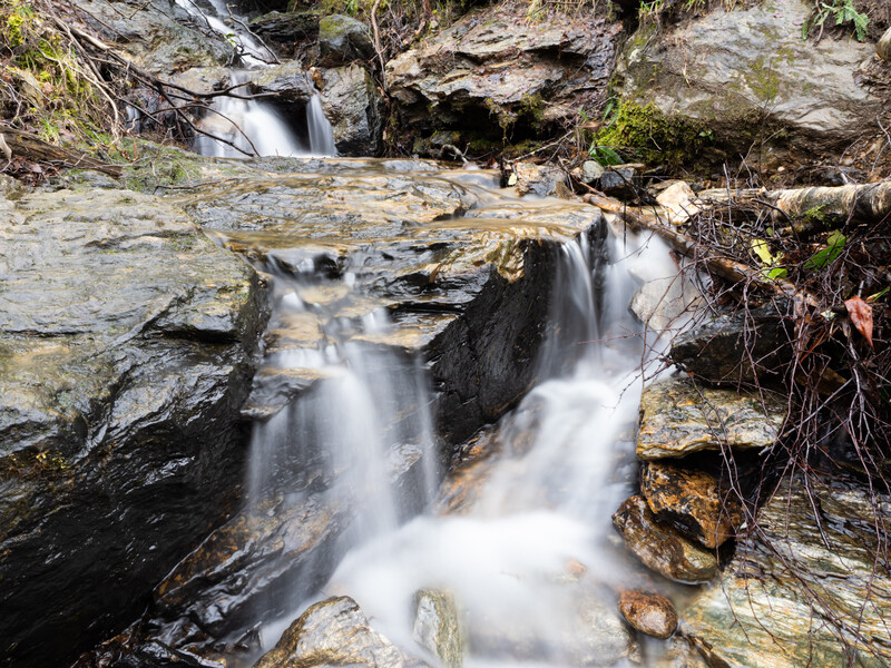 Small waterfall cascading over layered slate rocks with silky water motion blur effect.