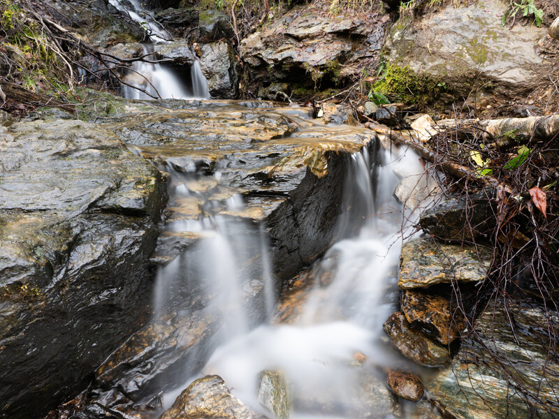 Cascading waterfall flowing over layered rock formations with long exposure blur effect.