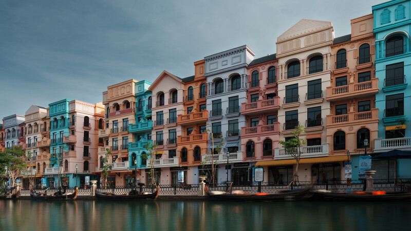 Colorful waterfront buildings in pastel shades of orange, blue, pink, and turquoise reflected in calm water.