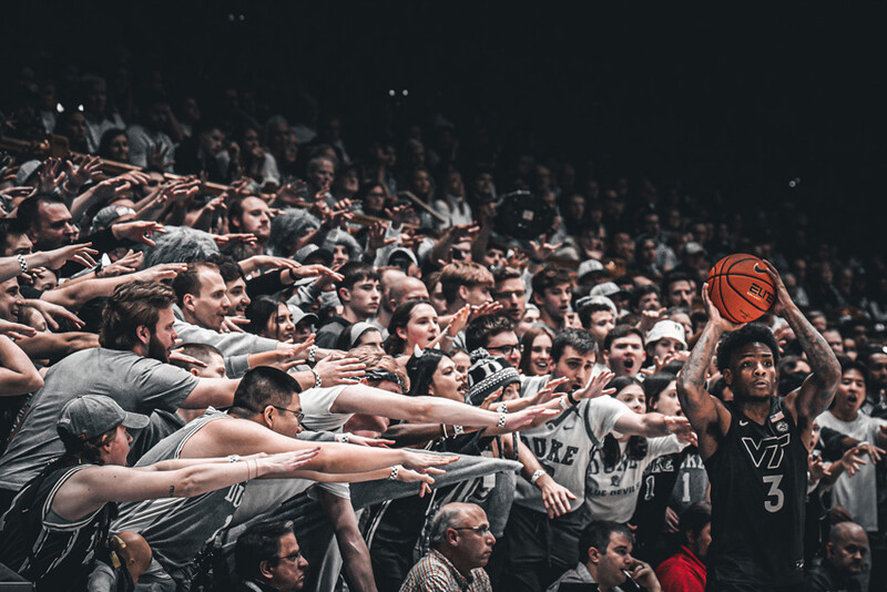 Crowd of spectators reaching toward a basketball player shooting during a game.