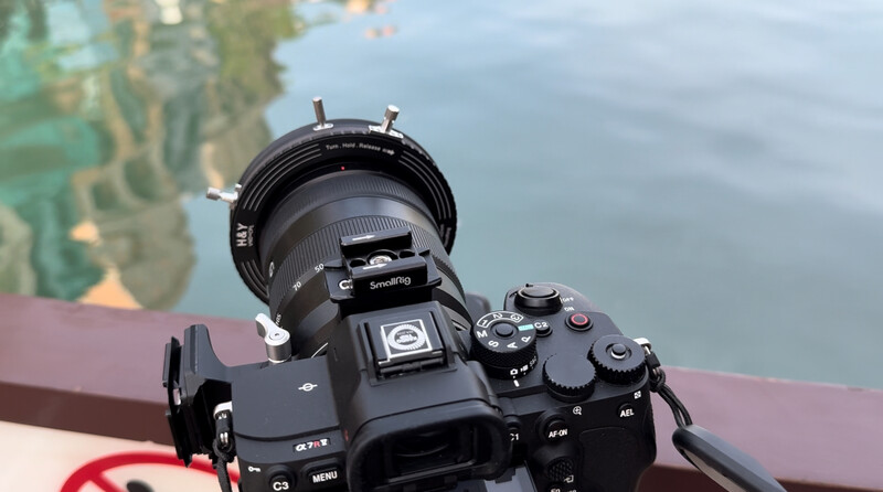 Mirrorless camera with telephoto lens mounted on tripod, positioned overlooking water with landscape visible in background.