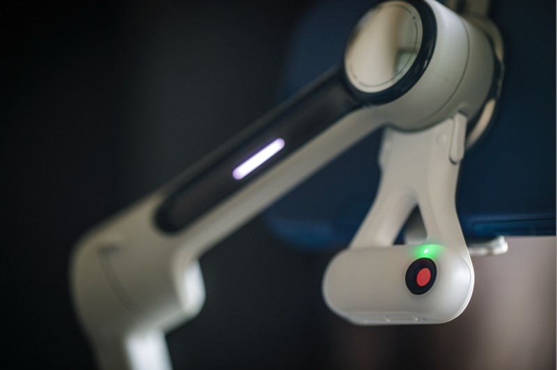 Close-up of a white robotic arm with illuminated control panel and red indicator light.