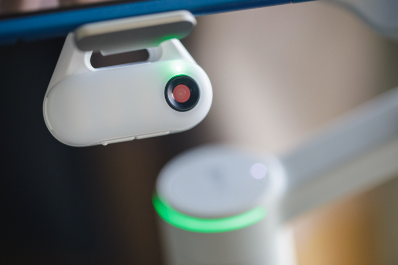 Dash cam mounted on vehicle windshield with illuminated green ring indicator and red recording light.