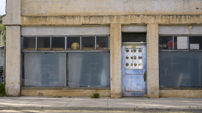 Weathered storefront with boarded windows, blue door, and peeling concrete facade.