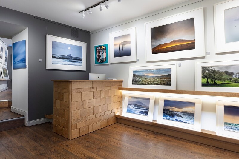 Photography gallery interior displaying framed landscape and seascape prints on dark and white walls.