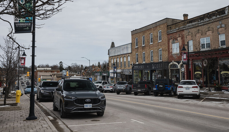 Main street lined with brick buildings and parked vehicles under overcast sky.