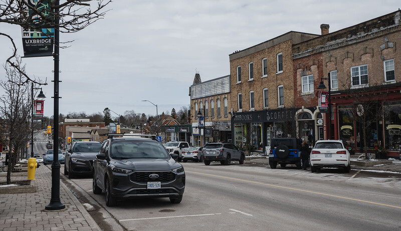 Street scene with parked cars and storefronts along a downtown main street on an overcast day.