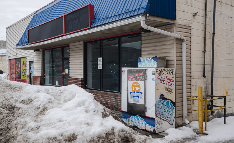 Abandoned storefront with snow drifts, boarded windows, and graffiti on a winter day.