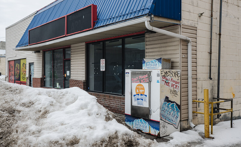 Abandoned storefront with boarded windows and graffiti covered by winter snow.