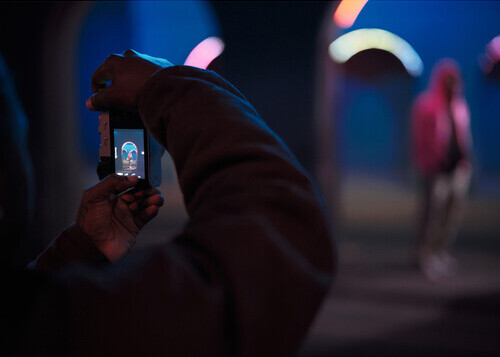 Person holding smartphone capturing scene with bokeh lights in background at night.