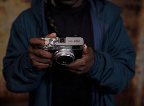 Photographer holding a vintage rangefinder camera with a silver body and manual focus lens.