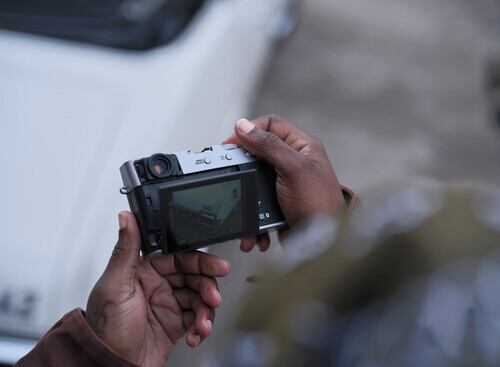 Photographer's hands holding a mirrorless camera with LCD screen visible during outdoor shoot.