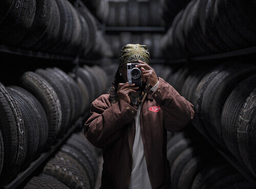 Photographer holding vintage film camera among stacked tires in an industrial setting.