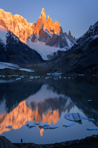 Alpine peak glowing orange at sunrise, mirrored in still lake water below.