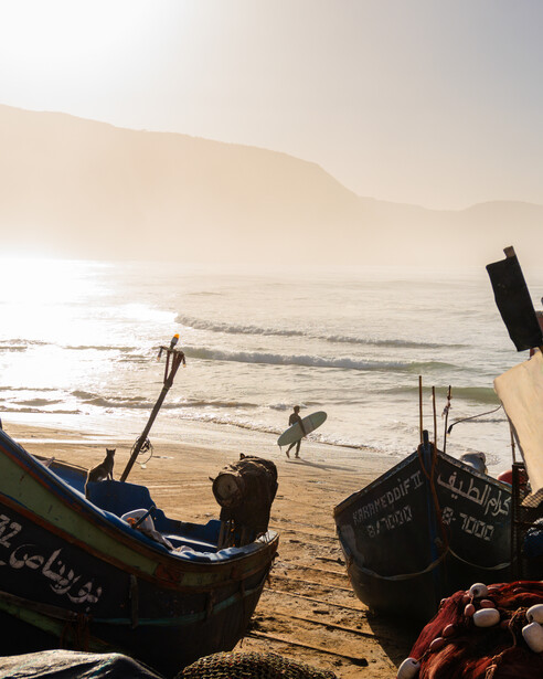 Fishing boats anchored in shallow water at a misty beach during golden hour.