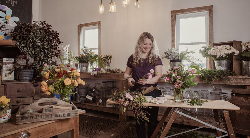 Florist arranging flowers at a wooden worktable in a bright studio with natural window light.