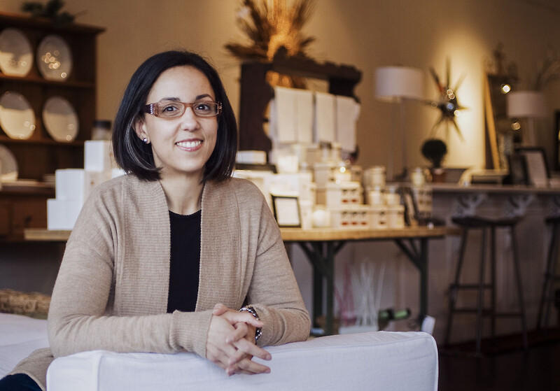 Woman with dark hair and glasses smiling at camera in a jewelry studio setting.