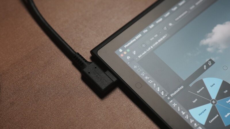 USB-C cable connected to the side of a tablet displaying photo editing software with adjustment panels.