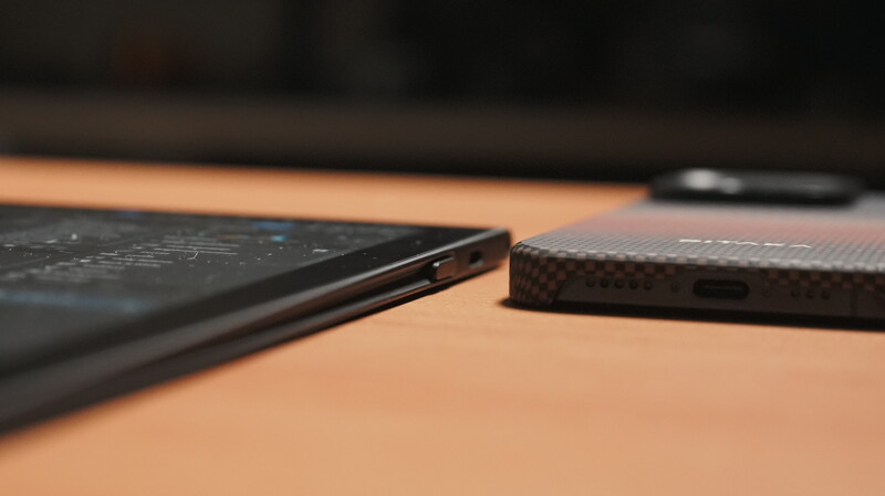 Close-up of two smartphones with dark cases on a wooden surface, showing ports and edges in sharp detail.