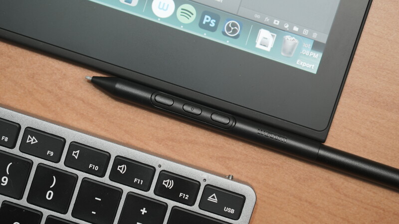 Stylus pen resting on a graphics tablet with keyboard visible below on wooden desk.