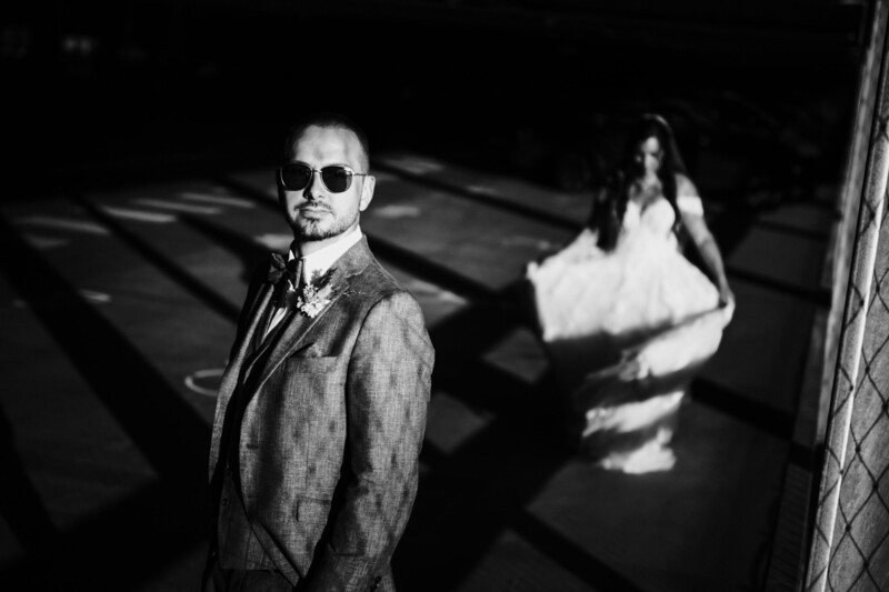 Bride and groom stand in a shadow pattern cast by a nearby fence