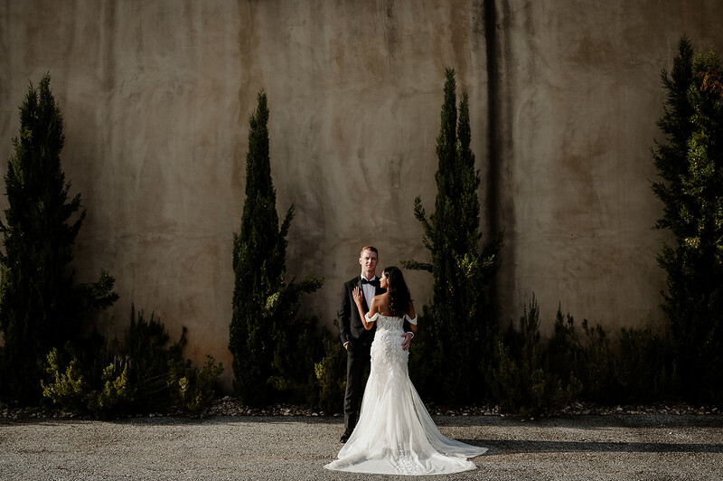 Bride and groom stand in front of a large wall