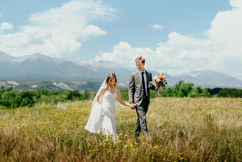 Married couple walks holding hands in an open field.