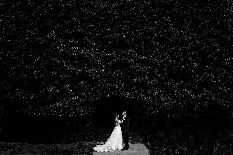 Bride and Groom pose in front of a wide shot of trees in black and white
