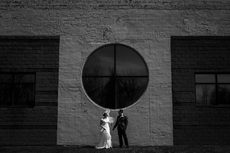 Bride and groom stand under hard light in front of a unique building