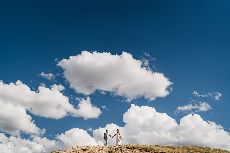 Bride and groom walk with large clouds in background for hard light portrait photography