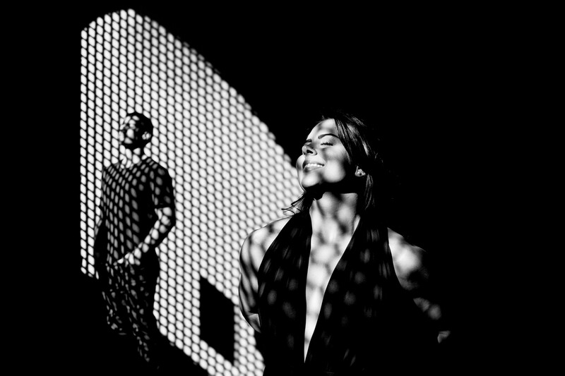 Man and woman stand in light with a shadow projected onto them