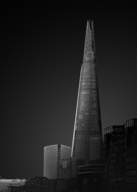 Tapered modern skyscraper rising sharply against dark sky, photographed from low angle in black and white.