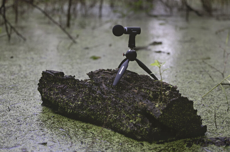 A small telescope mounted on a tripod positioned on a moss-covered log in shallow water.