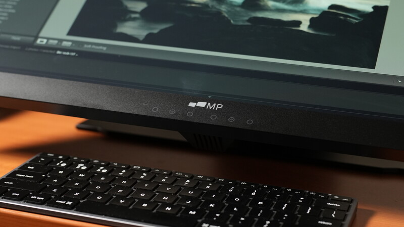 Computer monitor displaying image editing software above a wireless keyboard on an orange-toned desk.