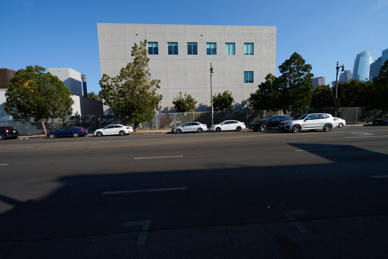 Modernist concrete building with parked cars along street under clear blue sky.